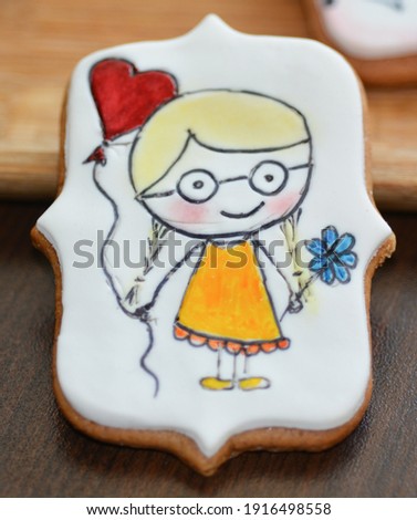 Cute blonde girl with glasses on an icing sugar for Valentine's Day. Honey cookies decoration