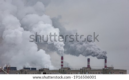 industrial chimneys with heavy smoke causing air pollution on the gray smoky sky background Royalty-Free Stock Photo #1916506001