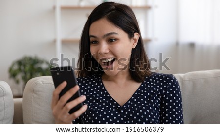 Shocked young mixed race female yelling looking at mobile phone amazed with pleasant surprise reward message. Excited millennial asian lady get super offer proposition from favorite web store by sms Royalty-Free Stock Photo #1916506379