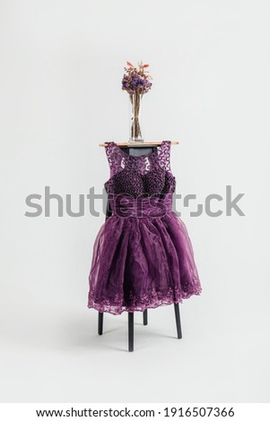 Purple sleeveless shiny dress hanging on wooden clothes rack isolated over white background.
