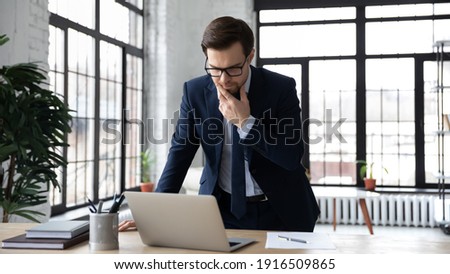 Pensive Caucasian businessman in suit work online on laptop think of business problem solution. Thoughtful male boss or CEO look at computer screen solve financial issue at workplace in office. Royalty-Free Stock Photo #1916509865