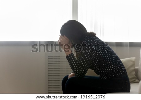 Desperate young woman sit on bed hiding face under palm having psychological problem difficult moment in life. Side shot of frustrated depressed female teenager lost in bad heavy thoughts. Copy space Royalty-Free Stock Photo #1916512076