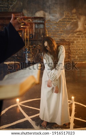 Exorcist in hood casting out demons from a woman Royalty-Free Stock Photo #1916517023