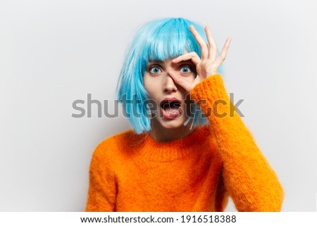 Studio portrait of happy young girl showing ok sign against white background. Wearing orange sweater and blue wig bob.