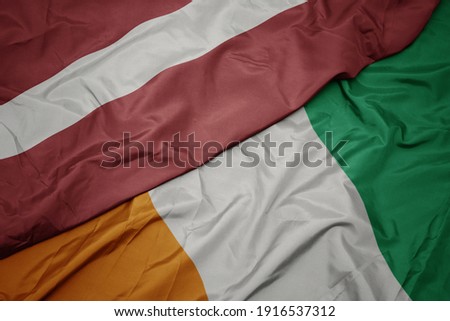 waving colorful flag of cote divoire and national flag of latvia. macro