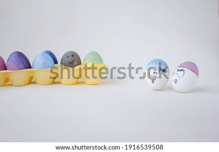 Multi-colored eggs on a yellow stand. Celebration and joy. Happy Easter. Hand-painted blue, blue, pink eggs. White egg with a funny face on a white background. Easter garland.
