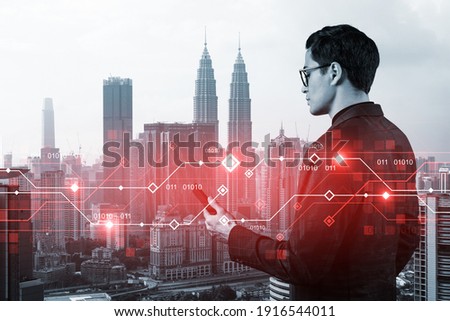 A handsome eastern businessman trying to achieve tremendous growth in commerce using new technological approaches by researching the internet in smartphone. Tech hologram icons over Kuala Lumpur