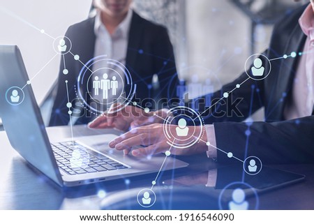Two HR specialists in formal wear analyzing the recruitment market using laptop to boost the intern program at international consulting company. Social networking hologram icons. Royalty-Free Stock Photo #1916546090