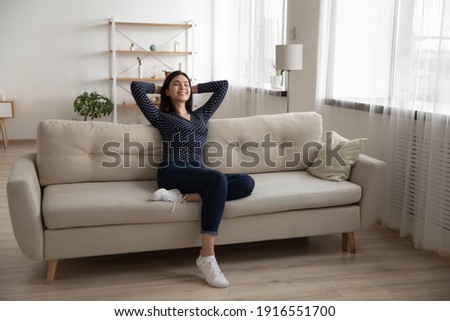 Young serene asian woman rest on soft stylish couch after finishing household chores enjoy tranquility feeling satisfied. Peaceful vietnamese lady chill at modern studio apartment breath fresh air nap Royalty-Free Stock Photo #1916551700