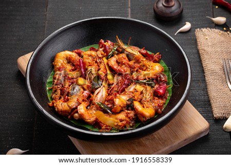  Kerala style Prawns roast or chemmeen varattiyathu  using red kashmiri chilli flakes and coconut slices as main ingrediants and garnished with onion rings and tomato slices ,placed on a black texture Royalty-Free Stock Photo #1916558339