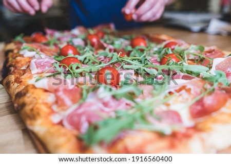 Chef hands preparing large pizza on wooden table. Preparing Parmesan, bacon, arugula pizza at restaurant