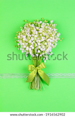 bouquet of lily of the valley flowers with a green bow and ribbon on a green background top view close up