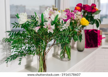 there are vases with different bouquets of flowers and a gift bag on the window. holidays and gifts concept