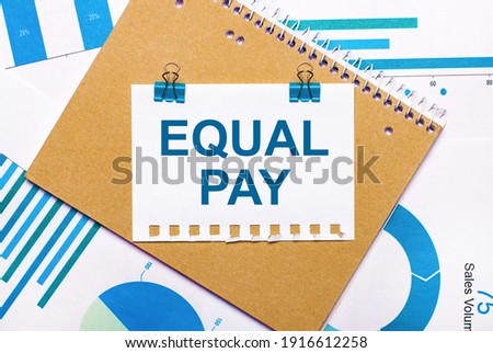 On the desktop are blue and light blue graphs and diagrams, a brown notebook and a sheet of paper with blue clips and EQUAL PAY text. View from above. Business concept