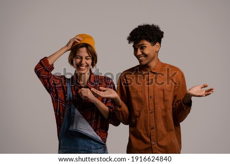 Photo of cute couple farmers laugh and look happy together . White woman wears denim overall, black man shirt isolated grey color background