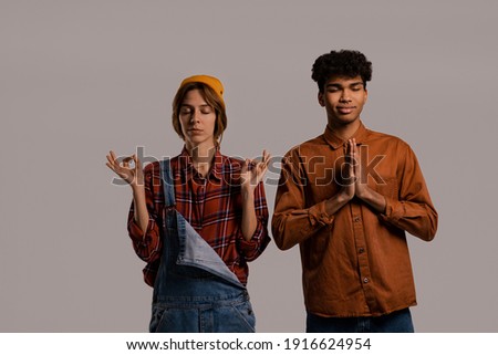 Photo of cute couple farmers meditate and have relax. White woman wears denim overall, black man shirt isolated grey color background