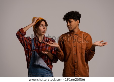 Photo of cute couple farmers look worried about something. White woman wears denim overall, black man shirt isolated brown color background