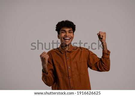 Photo of black man dances and has fun, smiles and looks happy. Male wears shirt, isolated grey color background