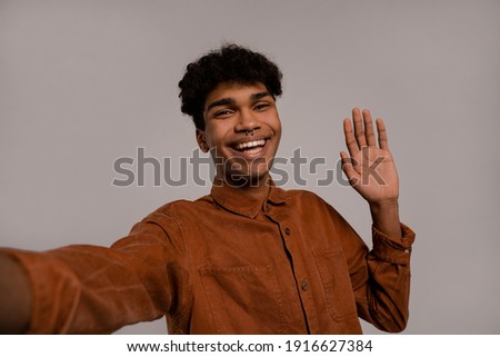 Photo of black man takes a selfie and smiles with perfect teeth. Male wears shirt, isolated grey color background