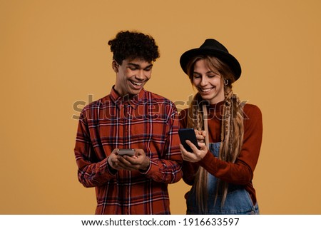 Photo of black male and white female farmers watch their smartphones. Man wears plaid shirt, Woman wears denim overall and hat isolated brown color background