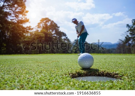 Blurred Golfer putting ball on the green golf, lens flare on sun set evening time. Golfer action to win after long putting golf ball in to the hole.                                 Royalty-Free Stock Photo #1916636855