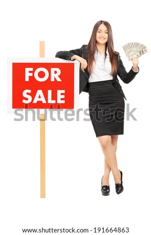 Female real estate agent holding money by a for sale sign isolated on white background