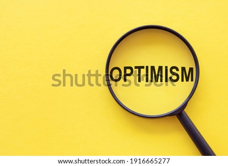 The word OPTIMISM is written on a magnifying glass on a yellow background.