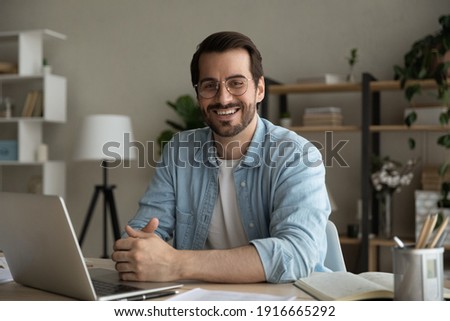 Profile picture of successful man worker employee college university student sitting by work desk at home office looking at camera. Portrait of motivated young guy studying working online using laptop Royalty-Free Stock Photo #1916665292