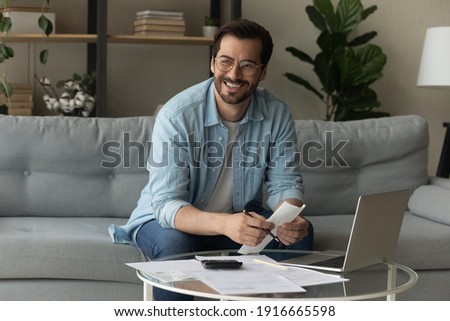 Happy young male distracted of studying terms conditions of credit documents look aside plan loan mortgage payments count on paper. Smiling man enterpreneur find legal way to cut costs get tax refund Royalty-Free Stock Photo #1916665598