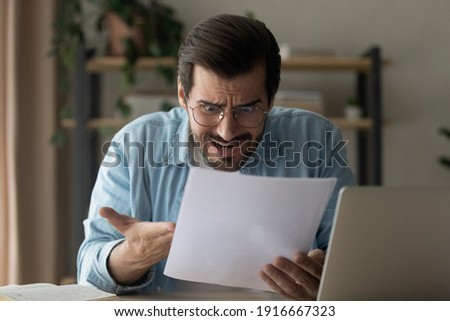 That is ridiculous. Angry frustrated guy freelancer feel panic look at official paper letter ordering to pay inexistent debt. Mad nervous young man read bad absurd conditions of loan proposed by bank Royalty-Free Stock Photo #1916667323