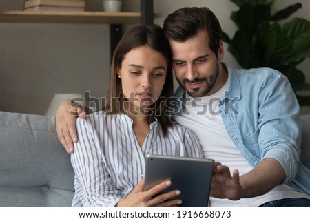 Focused married couple read insurance policy loan contract text from bank website on tablet screen planning to make treaty. Serious young spouses hold digital pad device buy goods order service online Royalty-Free Stock Photo #1916668073