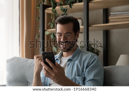 Great news. Overjoyed excited man in glasses read email from cell screen get awaited job offer invitation for interview. Happy young guy customer receive amazing offer bonus discount from online store Royalty-Free Stock Photo #1916668340