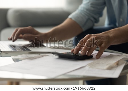 Close up of young male accountant hands make audit of expenses calculate charges based on paper documents. Cropped shot of man bookkeeper work with bills pay fees taxes online using web app on laptop Royalty-Free Stock Photo #1916668922