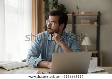Pensive young guy employee sit at workplace look aside of pc screen think on problem of research project. Thoughtful businessman analyze information ponder chances of success make calculations in mind Royalty-Free Stock Photo #1916668997