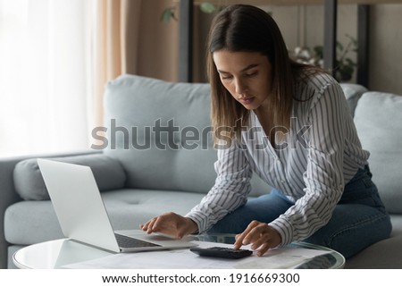 Attentive female student planning to pay college loan study financial papers count sum of regular payment to provide via electronic bank. Focused young businesswoman manage income calculate tax rates Royalty-Free Stock Photo #1916669300