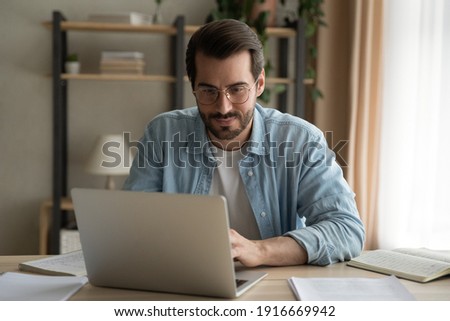 Attentive millennial male manager employee busy at telework at quarantine time study documents in corporate network from home pc. Concentrated young man specialist doing remote computer work on laptop Royalty-Free Stock Photo #1916669942