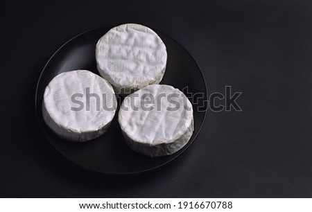 Three wheels of Camembert soft cheese on a black plate. Cheese with noble mold on black background.