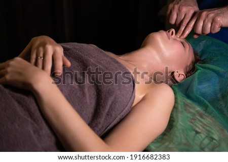 Professional facial massage. Male masseur makes procedures on a female face on a dark background