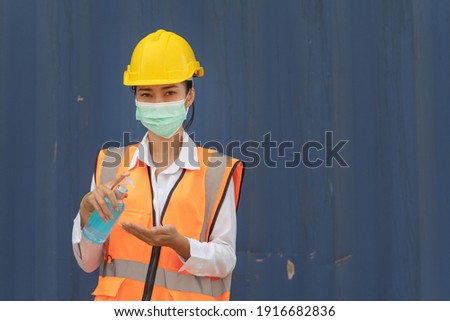 Asian Factory woman worker in a face medical mask and safety dress using alcohol gel for hand cleaning to protect coronavirus disease at blue wall.