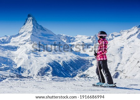 Happy female skier resting on top of the mountain observing nature at ski resort on a beautiful sunny winter day. Matterhorn. Swiss Alps