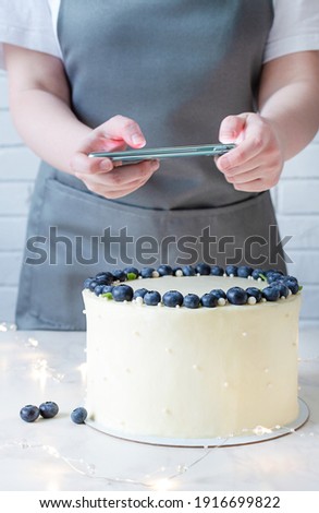 Professional food blogger taking pictures on smartphone. White cake with cream cheese and fresh blueberries