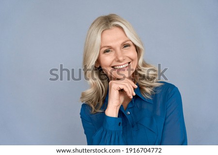 Smiling sophisticated 50s middle aged blond business woman looking at camera. Happy mature elegant old lady isolated advertising products or services on grey background. Headshot close up portrait