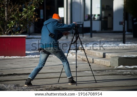 Portrait on back view of man taking a photo in the street with a tripod 