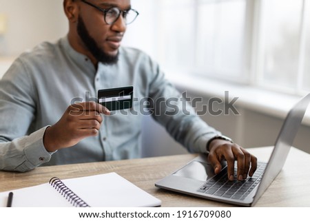 Black Businessman Holding Credit Card Using Laptop Shopping Online Sitting At Workplace In Office. Customer Making Payment, Banking Service, E-Commerce Concept. Selective Focus, Cropped