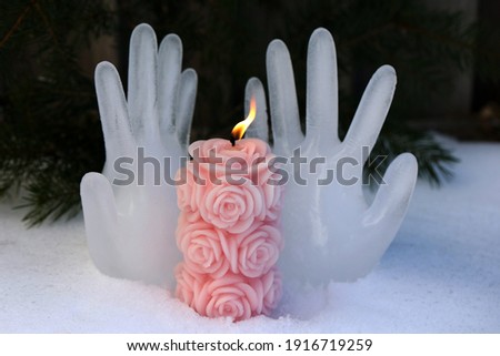 Burning candle on the background of hands made of ice.