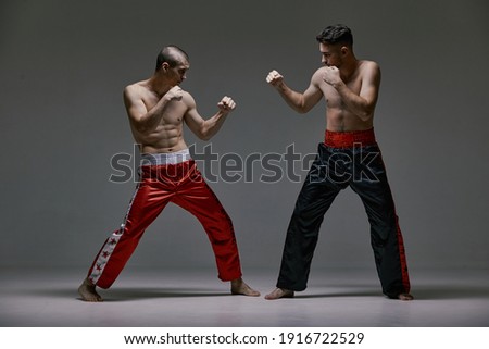 Boxers athletic guys fighting on gray studio background during kickboxing workout, mixed fight concept Royalty-Free Stock Photo #1916722529