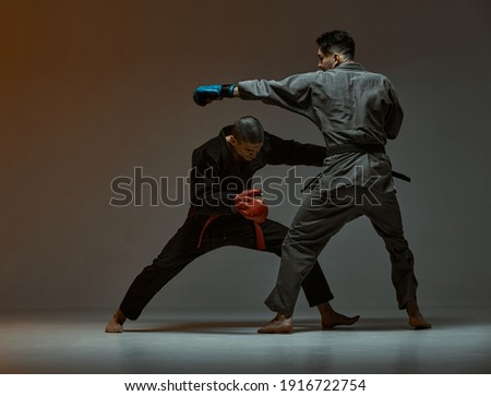 Sparring of two fighting guys wearing kimono and boxing gloves, mixed fight and martial arts concept