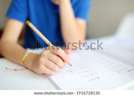 Elementary student boy doing homework at home. Child learning to count, solves arithmetic examples, doing exercises in workbook. Math tutorial. Preparing preschooler baby for school.Education for kids Royalty-Free Stock Photo #1916728130