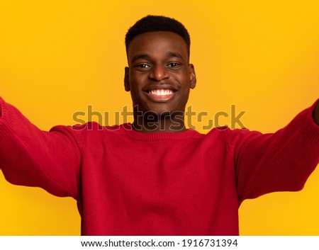 Selfie Time. Cheerful young african american guy making self-portrait and smiling at camera, positive black man taking photo standing isolated over yellow background, closeup shot with free space