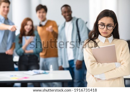 Bullying Concept. Rude diverse group of people mocking and making fun of sad woman in eyeglasses, pointing fingers at her and laughing, standing in blurred background. Prank, abuse, public disgrace Royalty-Free Stock Photo #1916731418
